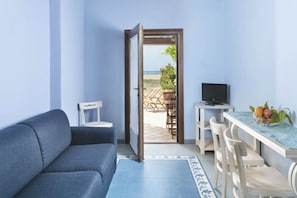 Una habitación con sofá, una mesa de comedor con sillas, televisión y vista a la playa.