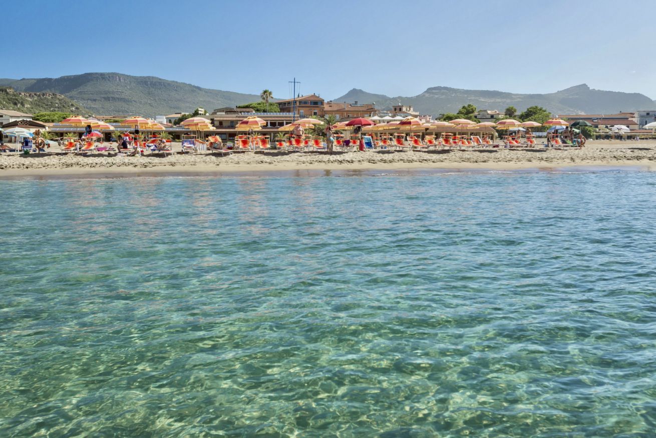 Een strand met helder water, parasols en ligbedden.