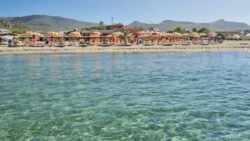 Een strand met helder water, parasols en ligbedden.