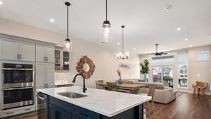 A modern kitchen with stainless steel appliances, a marble island, and pendant lighting. - Casita Miramar!: Semi-Oceanfront, Newly-Built Townhome, Community Pool! (Kill Devil Hills)