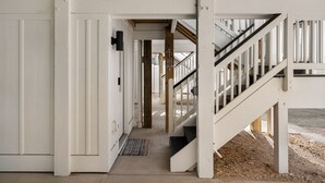 A hallway with white walls, a wooden door, and a staircase leading to an upper level. - Casita Miramar!: Semi-Oceanfront, Newly-Built Townhome, Community Pool! (Kill Devil Hills)
