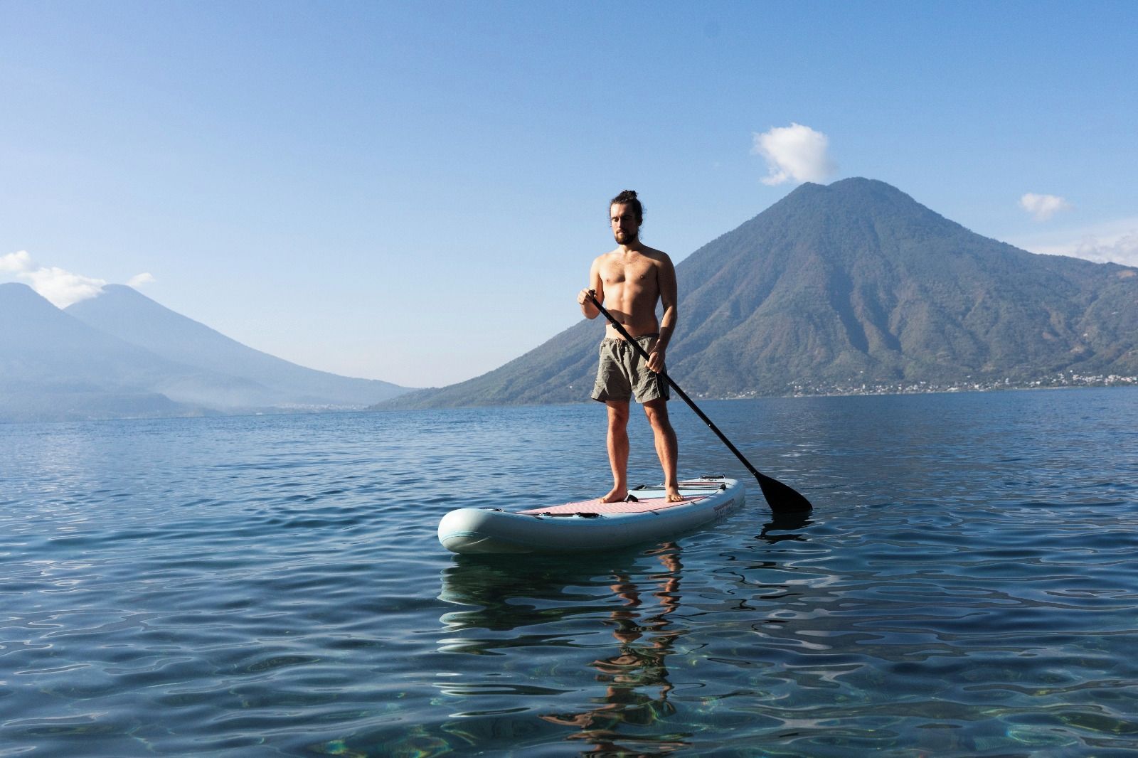 Une personne se tient debout sur une planche à pagaie dans une étendue d’eau, avec des montagnes en arrière-plan.