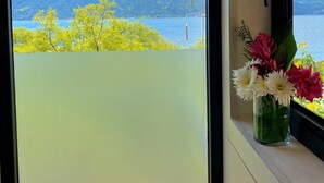 Vista dalla finestra su una montagna sullo sfondo, cielo sereno e un vaso di fiori sul davanzale.