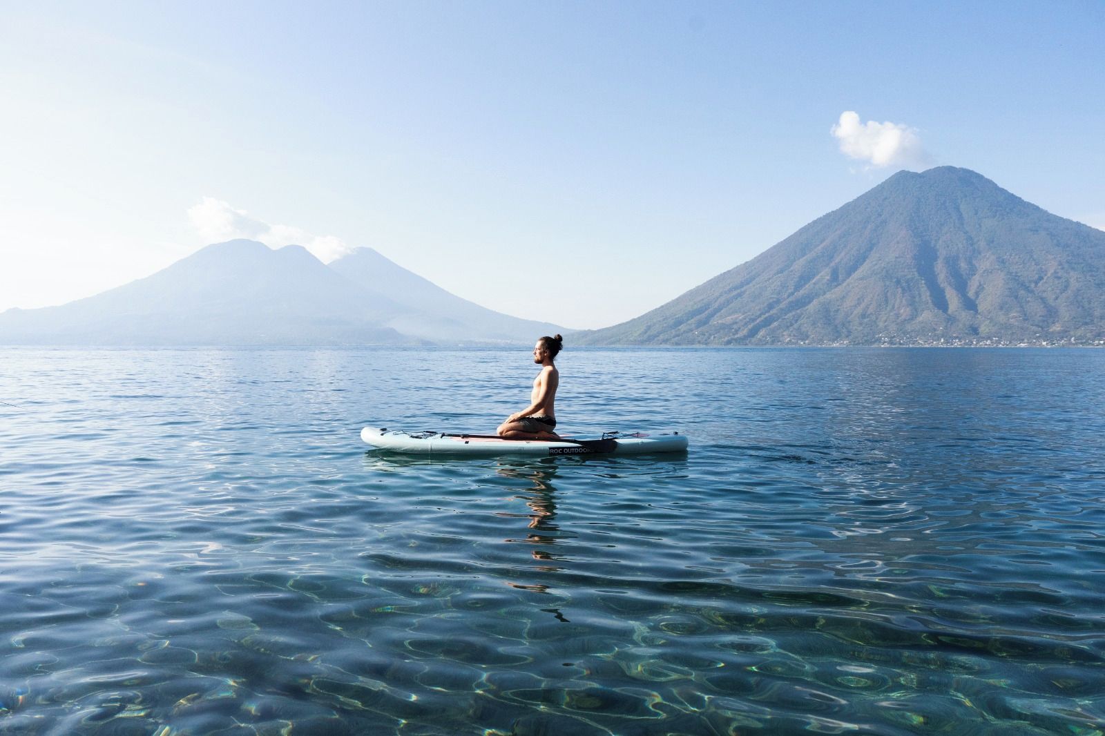 Una persona sentada en una balsa sobre aguas tranquilas, con montañas al fondo.