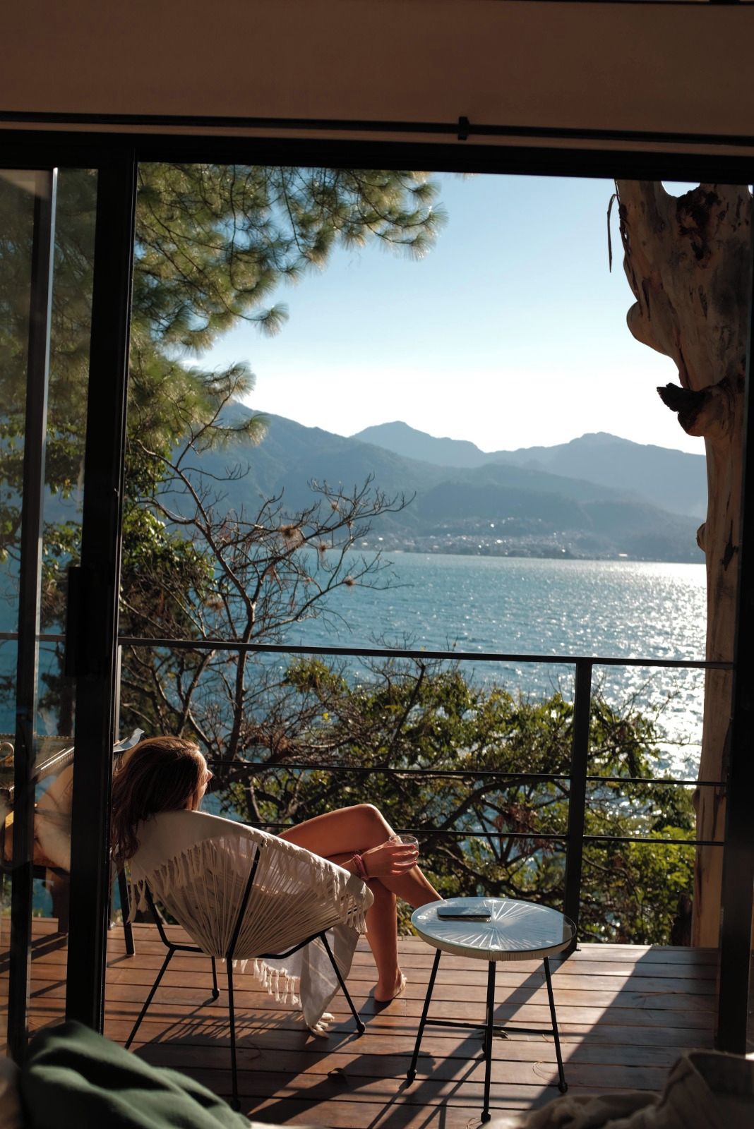 A balcony with a view of a lake and mountains, a chair, and a small table.