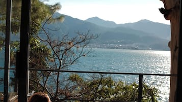 A balcony with a view of a lake and mountains, a chair, and a small table.