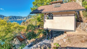Una casa moderna con una scala in pietra che conduce a un patio in legno, con vista su un paesaggio montuoso e uno specchio d'acqua.
