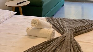 A hotel room with a green sofa, multiple pillows, a small round table, and a large window with a view of trees. - Nawa Beach - 106 by La Playa (Tamandaré)