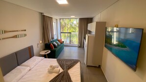 A hotel room with a bed, a sofa, a TV, and a balcony with curtains. - Nawa Beach - 106 by La Playa (Tamandaré)