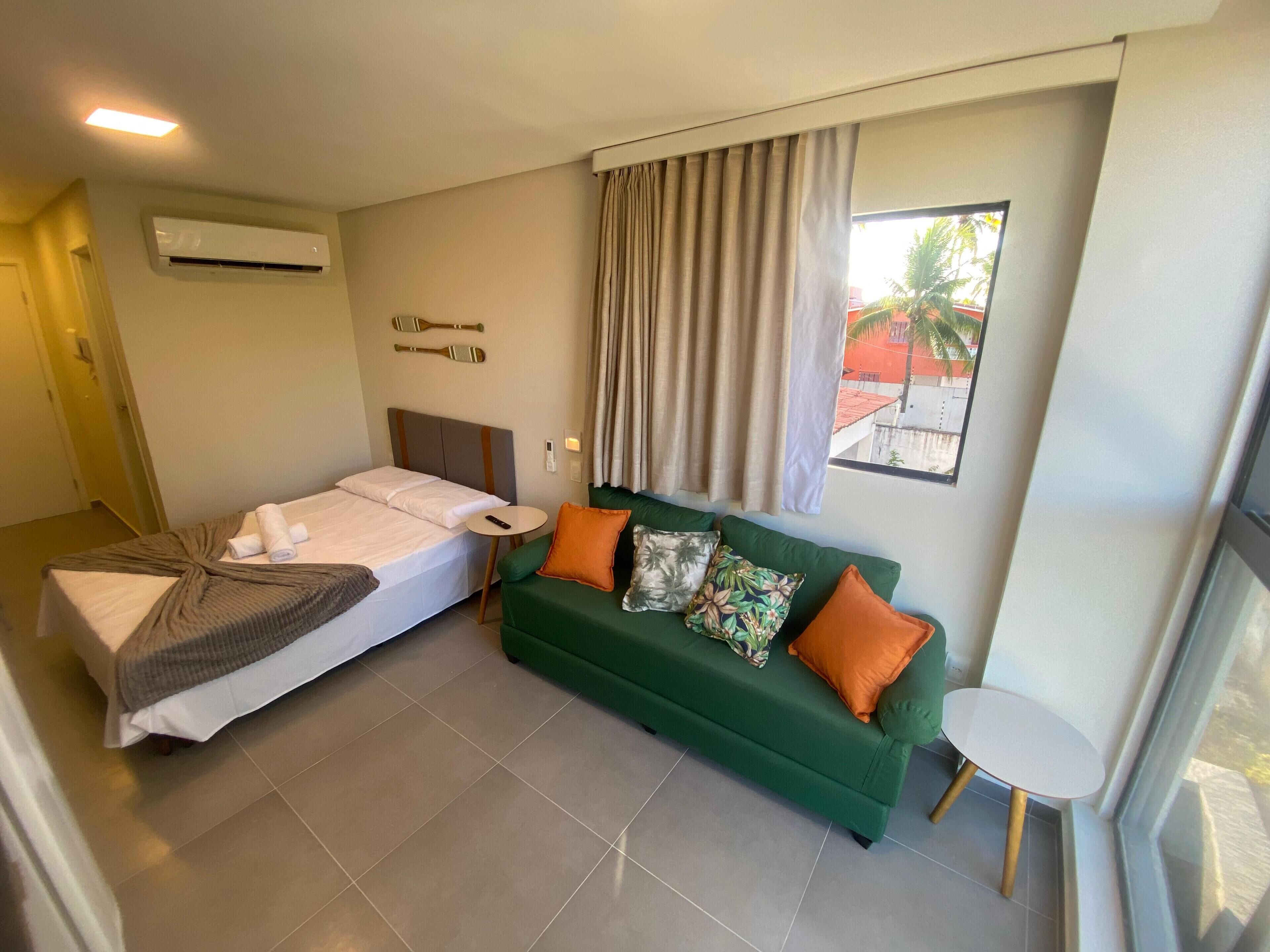 Una habitación de hotel con una cama, un sofá verde, una mesita y una ventana con cortinas.