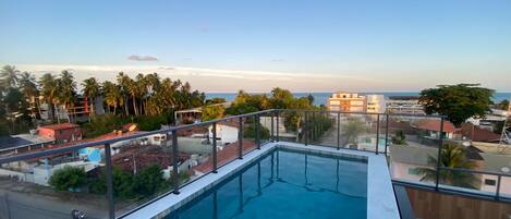 Una piscina en la azotea con vistas despejadas al mar y palmeras.