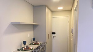 A narrow hallway with a small kitchen area featuring a table with chairs, a white cabinet, and a door at the end. - Nawa Beach - 106 by La Playa (Tamandaré)