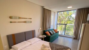 A hotel room with a bed, a green sofa, a window with curtains, and a ceiling light. - Nawa Beach - 106 by La Playa (Tamandaré)
