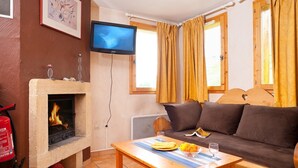 A cozy living room with a fireplace, a sofa, a TV, and a table with fruits and a glass. - Chalet privé et sympa 7p, ski aux pieds (Macot-la-Plagne)