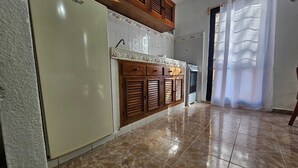 Cozinha com frigorífico, armários de madeira e chão em azulejo.