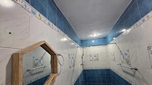 Casa de banho com azulejos azuis e brancos, espelho com moldura de madeira, chuveiro e sanita.
