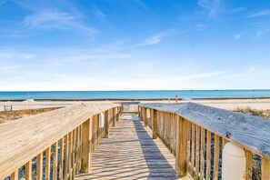 Une promenade en bois menant à une plage, avec un ciel dégagé.