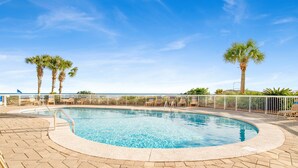 A swimming pool with a tiled deck, palm trees, and a view of the ocean. - Beachside @ Seaside Beach & Racquet 2BR Condo • Sleeps 6 • Pools, Tennis & Beach Access (Orange Beach)