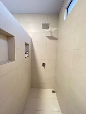 A narrow, tiled shower with a built-in shelf and a ventilation vent.
