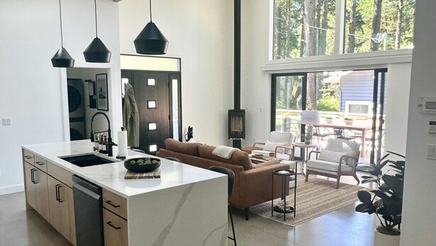 Une cuisine moderne dotée d’un îlot central, d’un coin repas avec un canapé et des chaises, et d’une grande fenêtre offrant une vue sur les arbres.