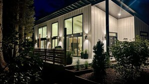 Une maison moderne dotée de grandes fenêtres, d’un porche abrité et d’un éclairage extérieur soigné la nuit.