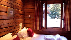 A cozy log cabin room with a bed, pillows, and a window with curtains.