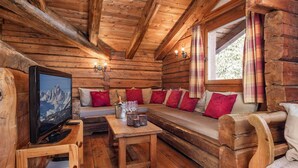 A cozy log cabin interior with a wooden sofa, a television, and a small table with glasses and a bottle.
