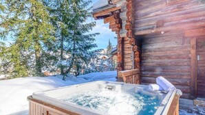 Una cabaña de madera con un jacuzzi en la nieve.