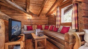Interior acogedor de una cabaña de madera con un sofá de madera, un televisor y una mesita con una botella y copas.