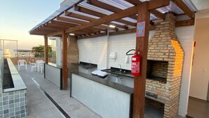 Un área de cocina al aire libre con horno de ladrillo, una pérgola y suelo de baldosas.