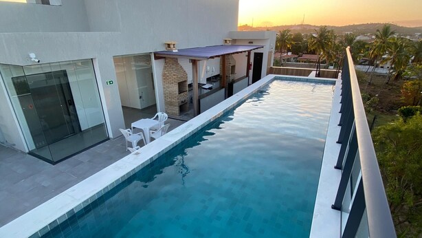 Un área moderna junto a la piscina con vista despejada al atardecer, un espacio de descanso techado al aire libre y un edificio con puertas de vidrio.