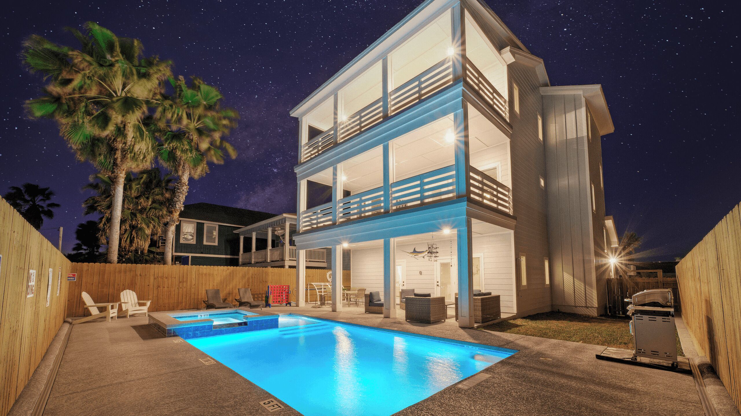A two-story house with a swimming pool, a wooden fence, and palm trees.
