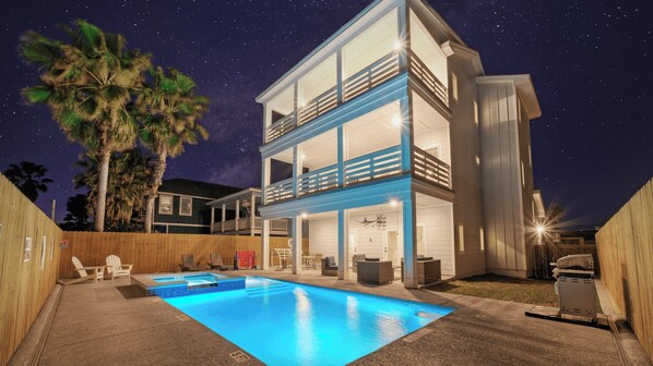Ein zweistöckiges Haus mit Swimmingpool, Holzzaun und Palmen.