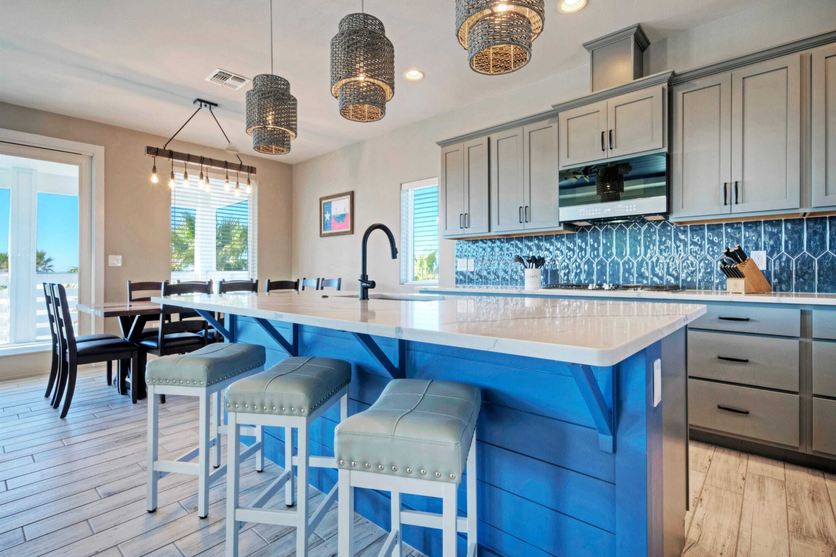 A modern kitchen with a large island, bar stools, pendant lights, and a backsplash with a blue pattern.