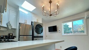 Una cocina moderna con armarios blancos, electrodomésticos de acero inoxidable, horno empotrado y un amplio ventanal.