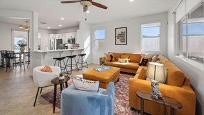 A modern living room with a sofa, armchairs, a coffee table, and a dining area with bar stools. - Casa Desert Muse: Heated Pool, Spa, Fire, Golf, Games, Pool Table, Art!

 (Indio)