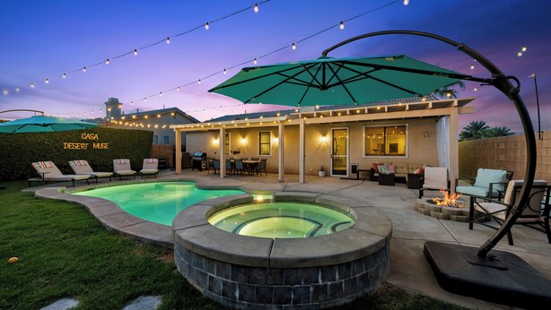 A backyard with a swimming pool, outdoor seating, and string lights. - Casa Desert Muse: Heated Pool, Spa, Fire, Golf, Games, Pool Table, Art!

 (Indio)