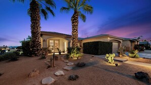 A residential property with a well-maintained garden, palm trees, and a garage. - Casa Desert Muse: Heated Pool, Spa, Fire, Golf, Games, Pool Table, Art!

 (Indio)