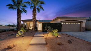 A residential property with a well-maintained garden, palm trees, and a garage. - Casa Desert Muse: Heated Pool, Spa, Fire, Golf, Games, Pool Table, Art!

 (Indio)