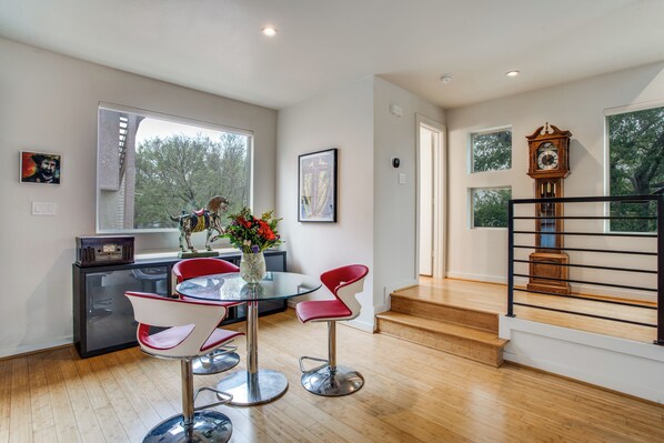 A modern kitchen with a glass dining table and red chairs, a clock on the wall, and a staircase leading to another level.