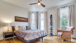 A bedroom with a bed, nightstand, lamp, ceiling fan, windows, and a chair.