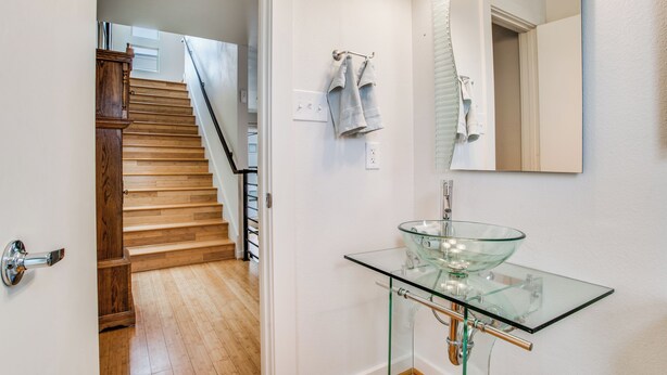 A modern bathroom with a glass sink, wooden stairs, and a mirror.