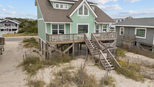 Una casa frente a la playa con un muelle de madera y escaleras que conducen a un balcón.