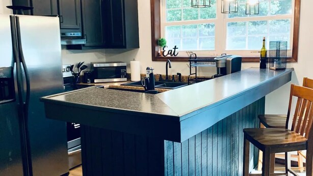 A modern kitchen with a central island, dark cabinetry, stainless steel appliances, and pendant lighting. - Charming Chalet at Pocono Ridge (Albrightsville)