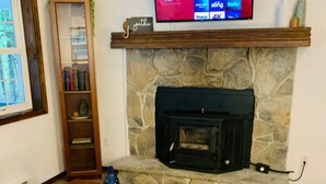 A living room with a stone fireplace, a mounted TV displaying streaming services, a wooden coffee table, and a sofa. - Charming Chalet at Pocono Ridge (Albrightsville)