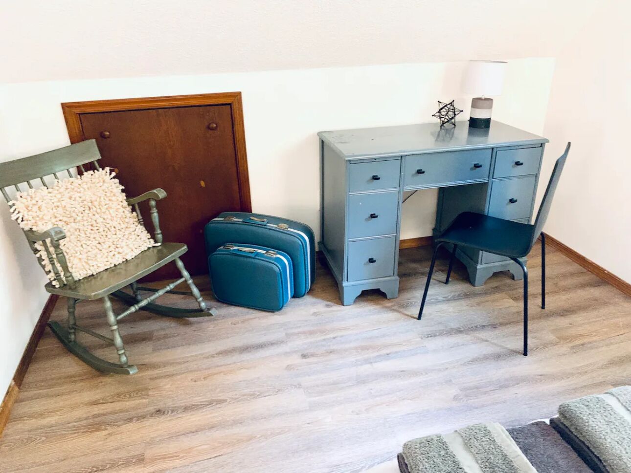 Een kamer met een schommelstoel, een bureau met een lamp en twee koffers.