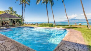 A swimming pool with a view of the ocean and mountains, surrounded by palm trees and lounge chairs. - Sun-Kissed Retreat with Oceanfront Views (Lahaina)