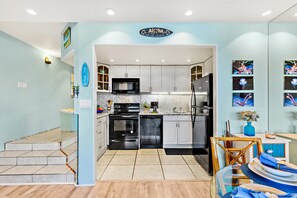 A modern kitchen with white cabinets, a black microwave, and a stainless steel refrigerator.
