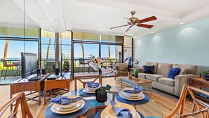 A modern living room with a dining area, large windows, and a ceiling fan. - Sun-Kissed Retreat with Oceanfront Views (Lahaina)