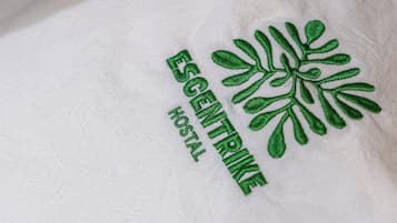 Tejido blanco con bordado verde que muestra las palabras 'ESGENTRIKE HOSTAL' y un diseño de hoja verde.